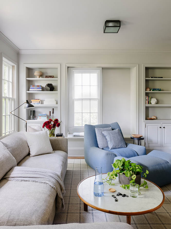 Family room with soft grey walls and ceiling, grey sectional, blue accent chair and ottoman, walnut and marble coffee table, and black light fixture.