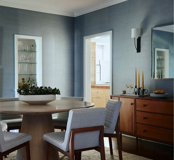 Blue grasscloth wallcovering in a formal dining room featuring a cerused oak pedestal table, upholstered side chairs, a mid-century console, and abstract art.