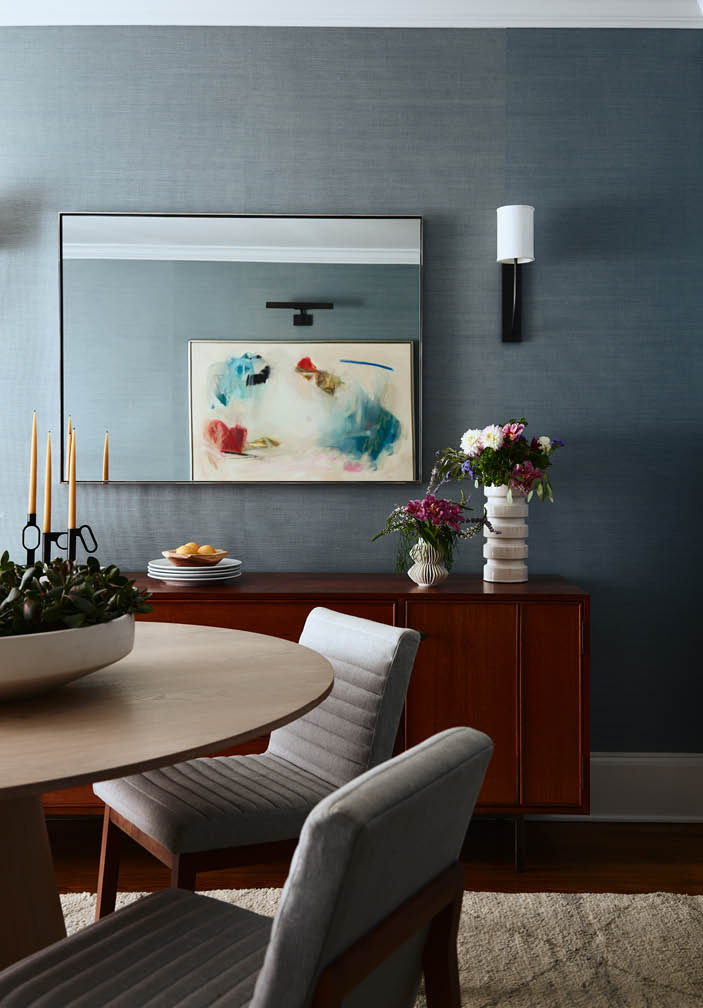 Formal dining room with blue grasscloth walls, modern lighting, a cerused oak pedestal table, mid-century console, and bold abstract artwork.