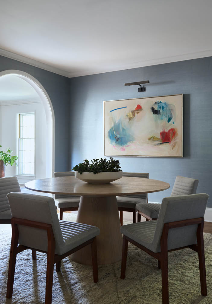 Mid-centuryinterior design dining room with a blue grasscloth backdrop, a cerused oak table, upholstered chairs, abstract art, and contemporary lighting.