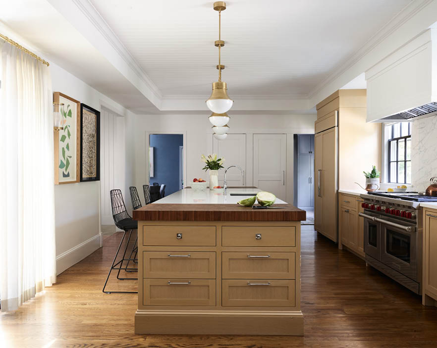 Kitchen with natural oak cabinets, walnut butcher block end, brass pendants, custom linen drapery, contemporary art, and no upper cabinets.