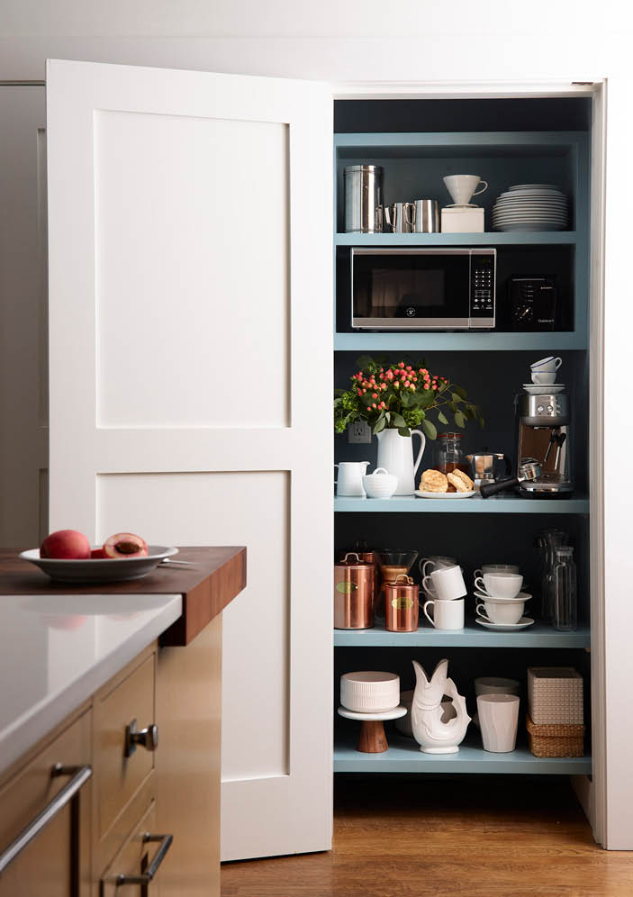 Custom blue pantry hidden behind a door in a kitchen with a natural oak island and walnut butcher block, featuring a niche for espresso and microwave.