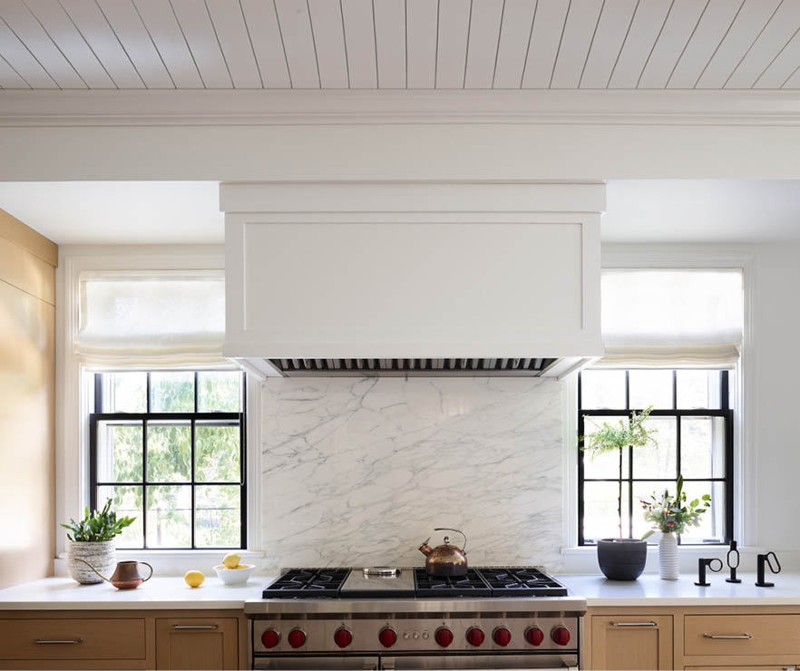 Kitchen with natural oak cabinets, white hood, shiplap ceiling, white Carrera backsplash, and simple elevation featuring a 48" wide Wolf range.