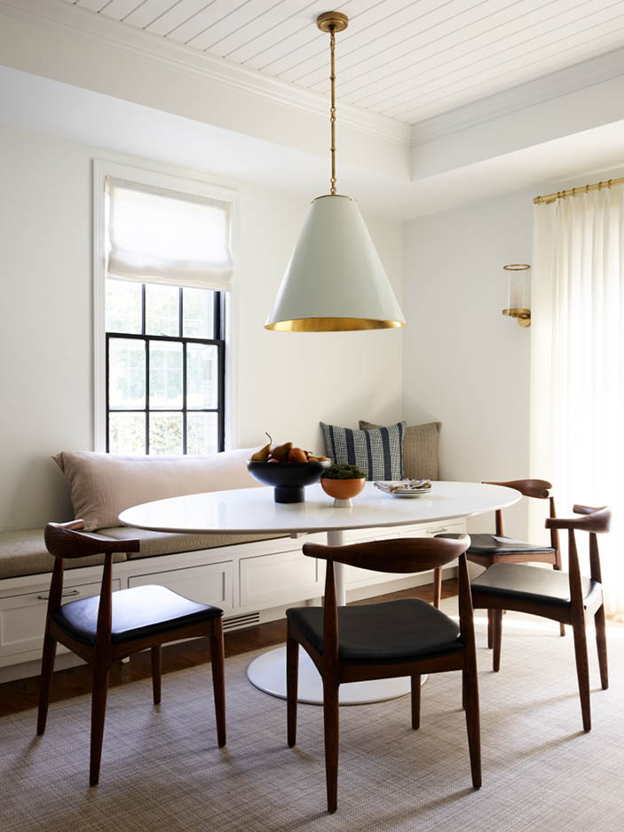 Breakfast nook with mid-century modern table, chairs, custom white bench seating, shiplap ceiling, custom cushions, pillows, and white linen drapery panels.