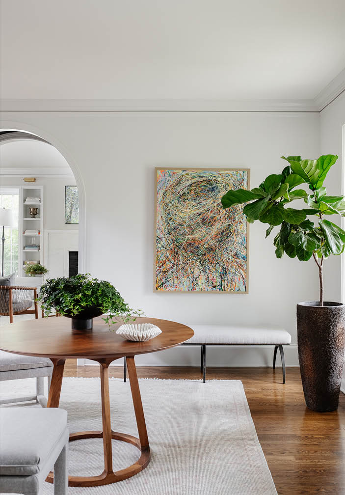 Arched entryway leading to formal living room in historic Hingham home, featuring a walnut table, custom art, neutral furnishings, and a marble fireplace.