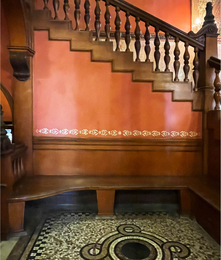 Staircase inside Flagler College with a built-in bench, mosaic flooring, and intricate architectural details in the stringer, spindles, and handrails.