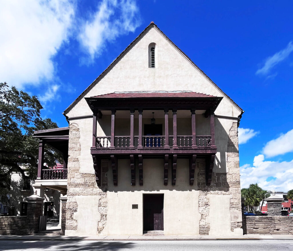 Historic stucco and stone home with an original wood door and a second-floor balcony featuring unique architectural details and sun coverage.