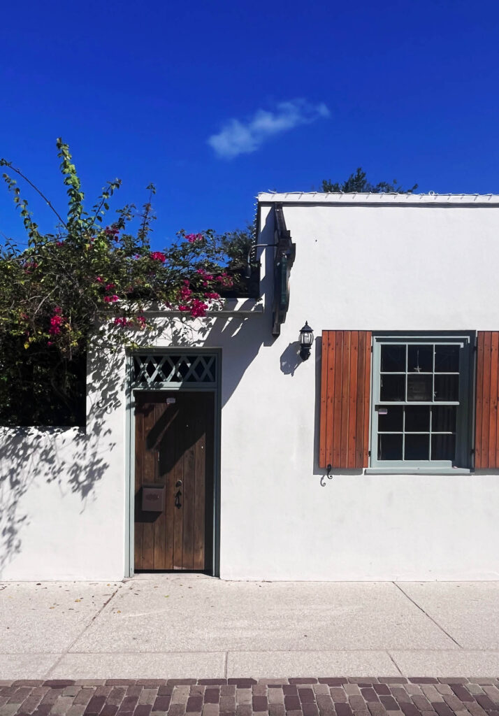 Charming entry to a private home in St. Augustine, Florida, with bright white stucco, historic wooden shutters with aged paint, and a wood door.