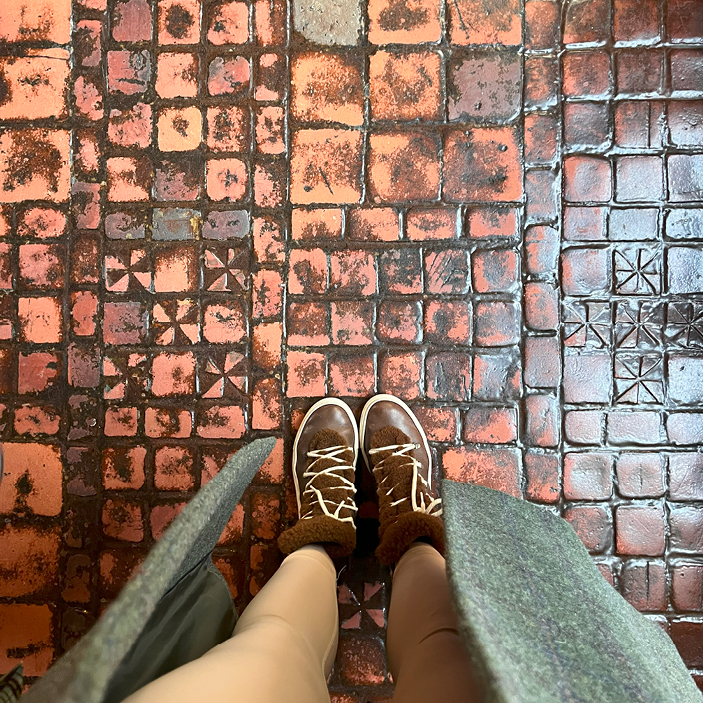 Sarah in beige leggings, a green coat, and sherpa sneakers, looking at historic tiles at the Isabella Stewart Gardner Museum in Boston, offering Boston Interior Design Inspiration. 