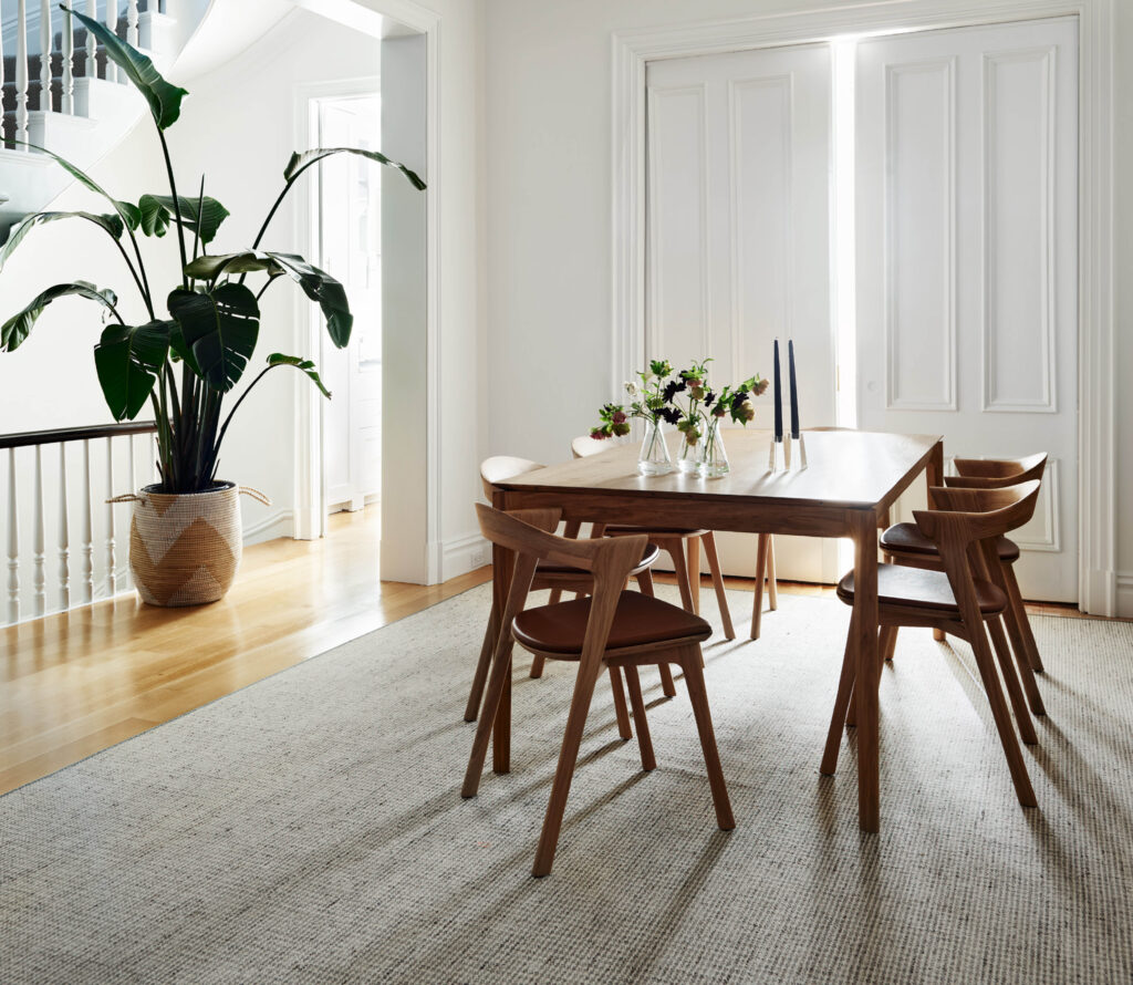 Brownstone interior design by Sarah Scales Design Studio featuring a dining table, houndstooth rug, original millwork, and a historic staircase.