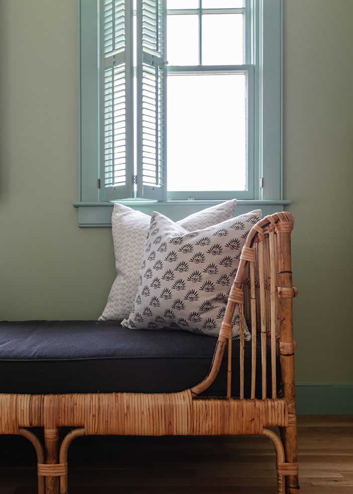 Guest bedroom in a beach home featuring a rattan daybed, custom pillows, and walls and trim in soft green and blue. Designed by Boston interior designer Sarah Scales, this space highlights coastal and New England interior design with a playful touch.