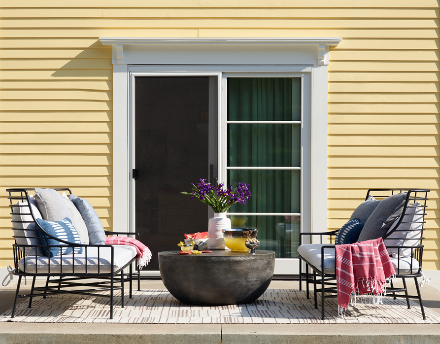 Small deck off the kitchen of a historic Hingham home with a classic yellow exterior, featuring space for facing sofas and a small table. New sliding doors connect the kitchen to the outdoor area, reflecting New England interior design.