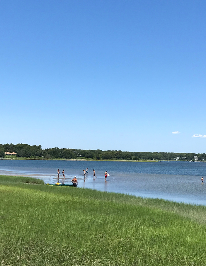 Bayside in Falmouth, local kids play in serene waters, capturing the effortless beauty and inspiration for a Boston interior designer’s New England design.