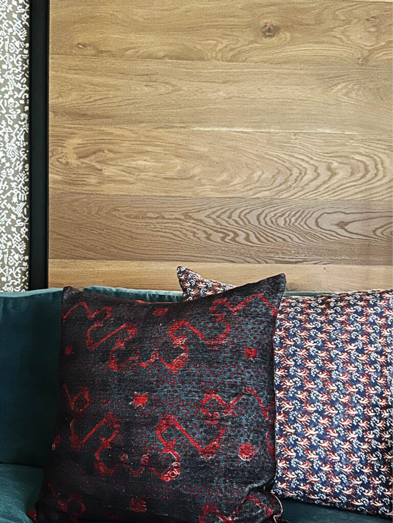 A wood barn door with exposed metal hardware, Zak & Fox wallpaper, a teal velvet sofa, and custom pillows in a Vermont ski house family room.