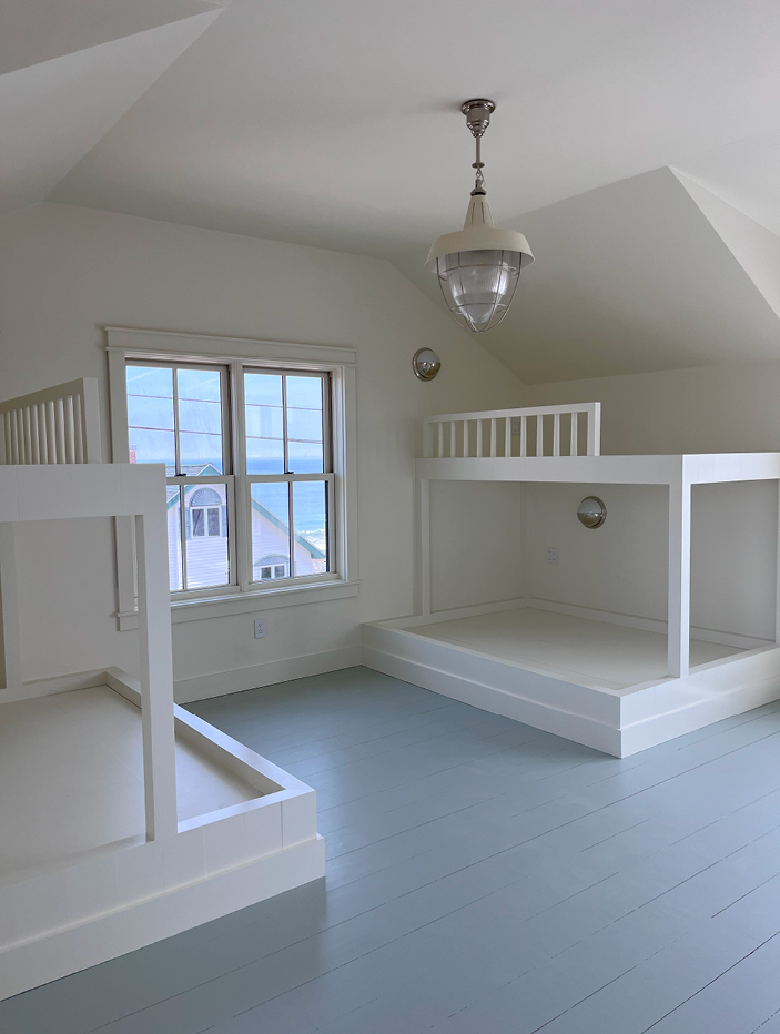 Custom daybeds with blue floors, white bunk beds, and nautical light fixtures in a Boston South Shore beach house.