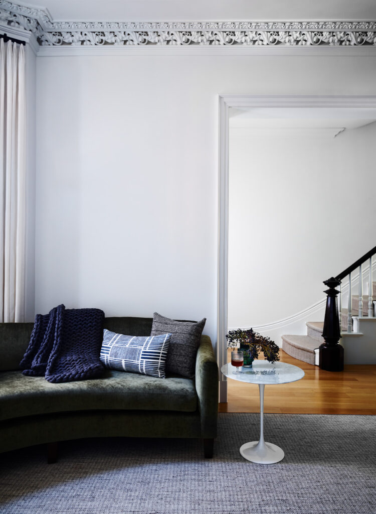 Modern living room with custom dark green curved sofa, mid-century table, and houndstooth rug in a historic Boston brownstone by Boston design firms.