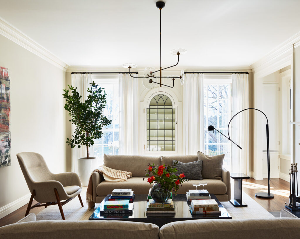 Modern living room with beige walls, contemporary furniture, and a Visual Comforts chandelier by a Boston interior decorator.