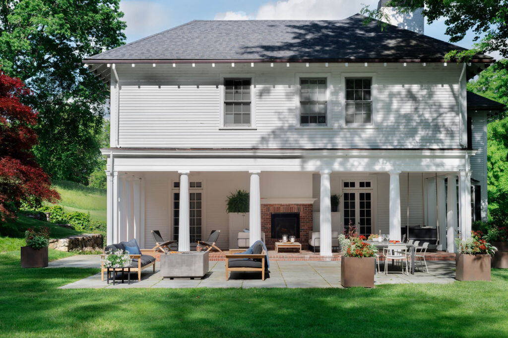 Covered porch with wood-burning fireplace, bluestone patio with gas firepit, and modern furniture at a historic Concord home.