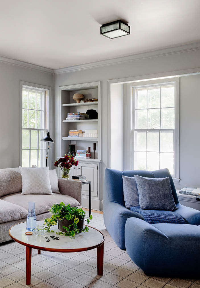 Family room with soft grey sectional, blue chair and ottoman, mid-century coffee table, and simple lighting by a Boston area interior designer.