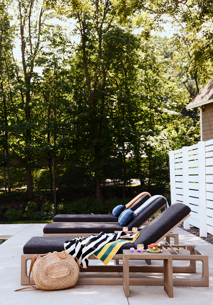 Modern lounge chairs with black cushions, small side table on a concrete patio at a pool in a historic Hingham home by a Boston interior designer.