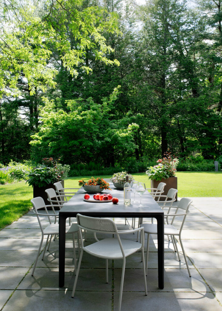 Bluestone patio with a Gloster dining table and stackable Blu Dot chairs for outdoor dining at a historic Concord home.