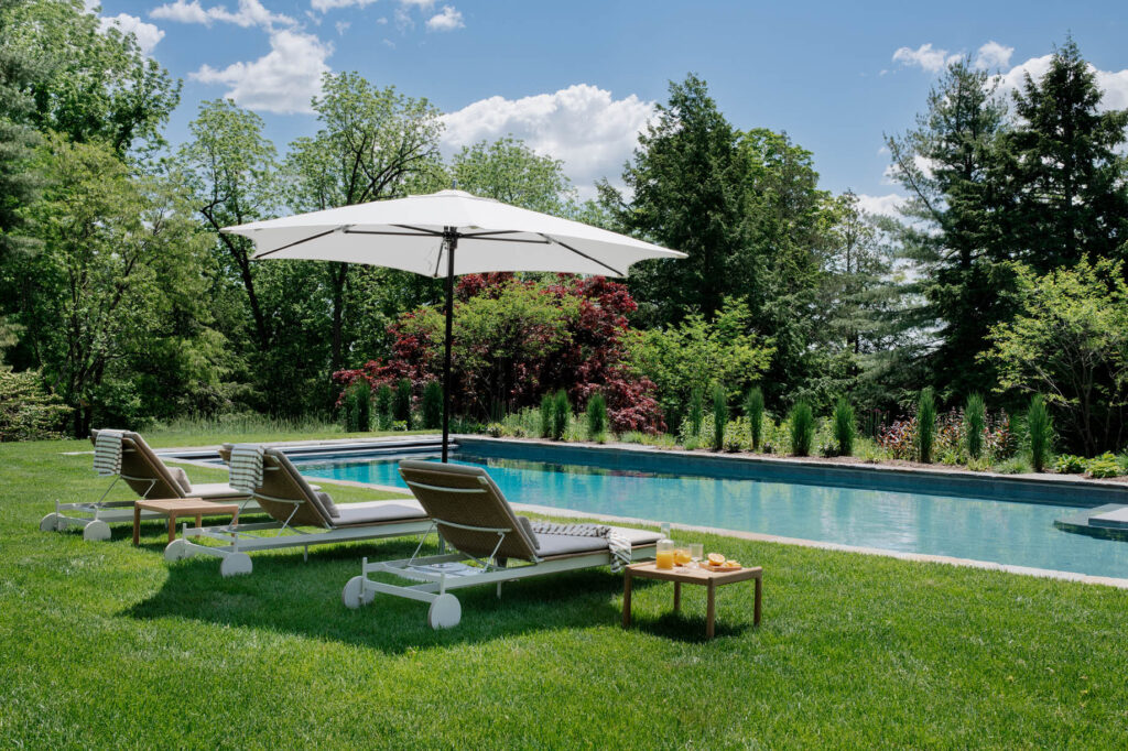 Modern pool design at a historic Concord home with contemporary outdoor furniture, selected by Boston interior design firms.