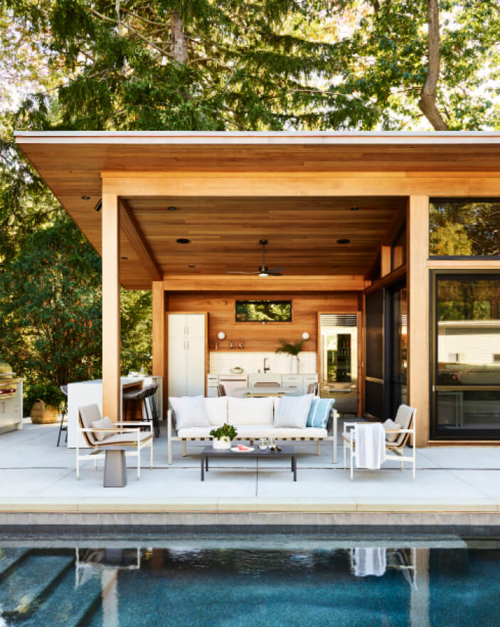 Covered outdoor kitchen with lounge furniture at a modern Hingham pool house next to the pool, by Hingham interior designers.