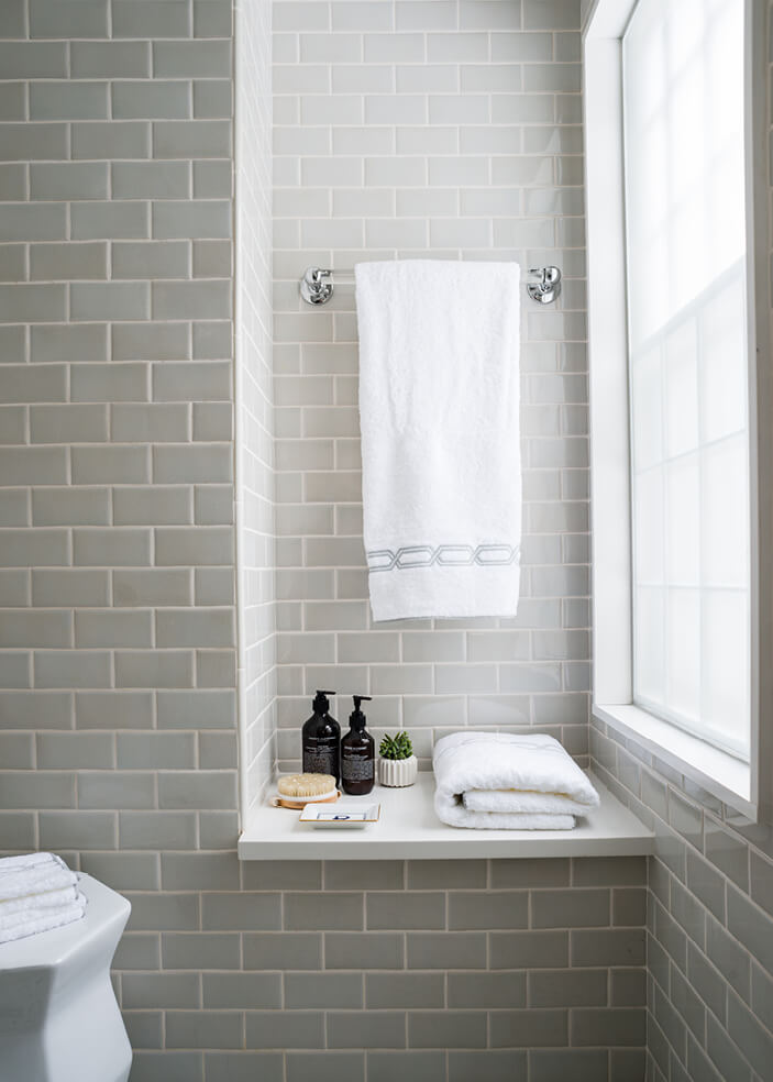 A Dover bathroom renovation with custom light grey ceramic tile, a bench, and polished nickel accessories. Designed by a Boston interior designer.