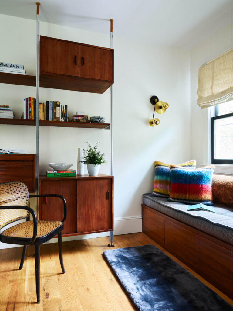 A retro heirloom desk beside a walnut window seat with a custom Gastón y Daniela tufted mattress, Pierre Frey pillows, and a navy shearling rug.