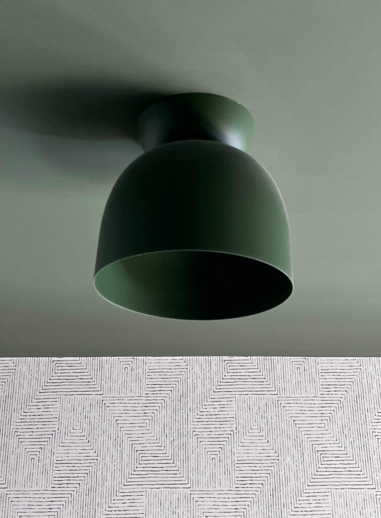 A green Cedar & Moss light fixture against a green ceiling with white and green geometric Kravet wallpaper in a basement kids' bedroom design.