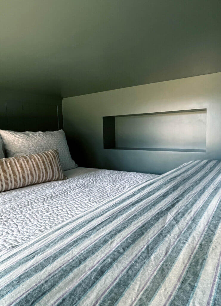 Custom dark green bunk beds in a Vermont ski house with striped linen bedding, textured layers, and Zak & Fox yellow pillowcases.