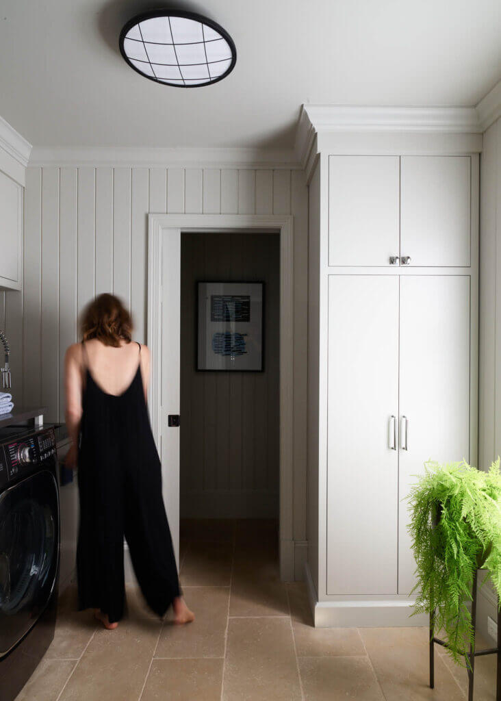 Custom cabinets in the laundry room of a historic Hingham home with limestone floors, shiplap walls, and a doorway leading to a powder room.