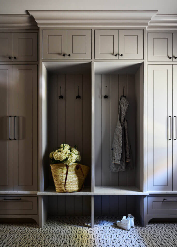 A custom mudroom with light grey inset cabinets, beaded doors, oil-rubbed bronze hardware, and black, white, and grey mosaic flooring.