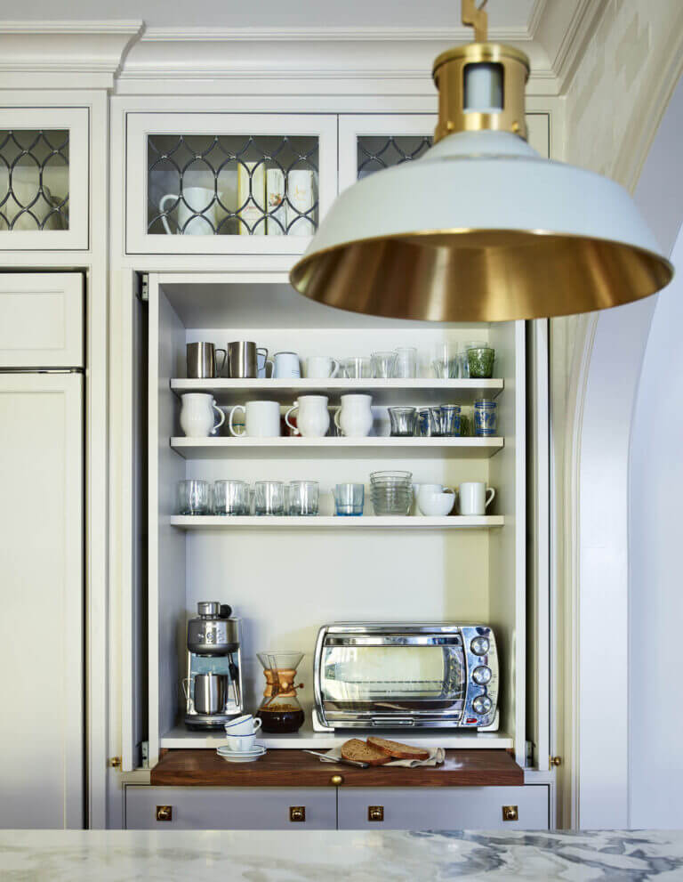 A custom breakfast nook cabinet with pocket doors concealing outlets, a toaster, and a coffee maker. Mirrored backsplash in kitchen with leaded glass details and brass accents.