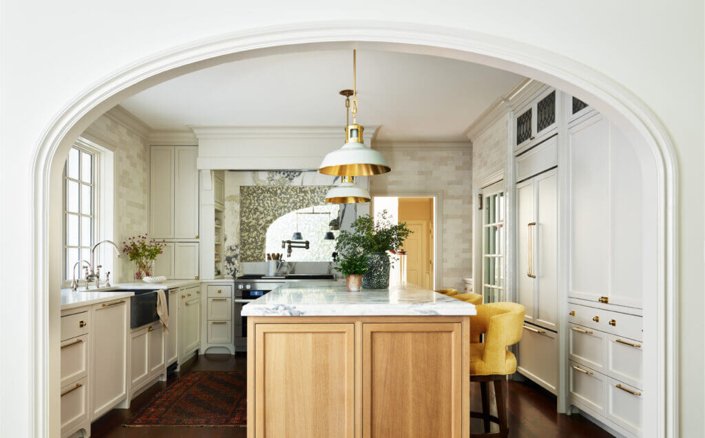 Classic aesthetics in a Milton kitchen with a natural oak island, soft white cabinets, custom brass fixtures, and a mirrored backsplash. 