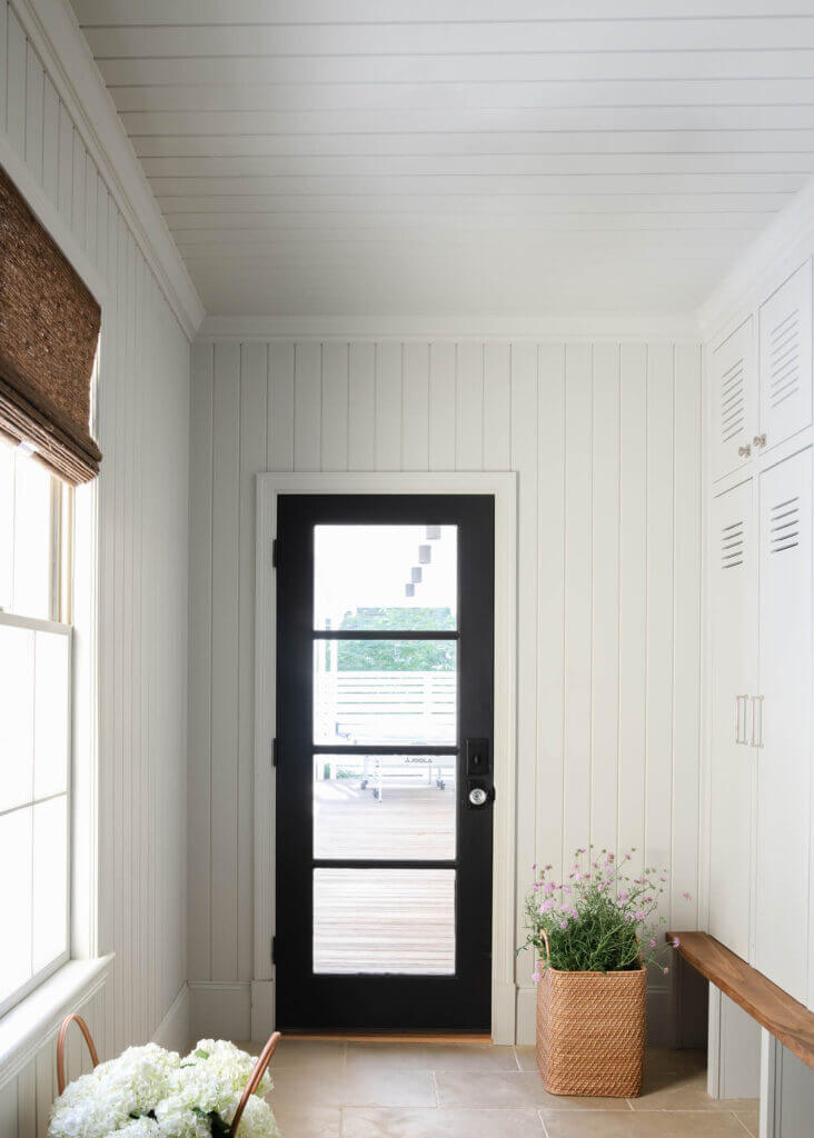 Custom light grey mudroom cabinets with shiplap walls, a black door to the back deck, and limestone flooring by Hingham interior designers.