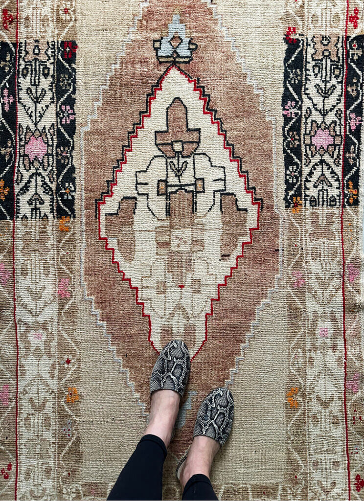 A vintage area rug in a Vermont ski house, paired with Emerson Fry snakeskin slides. Travel inspiration for interior design with layered textures.