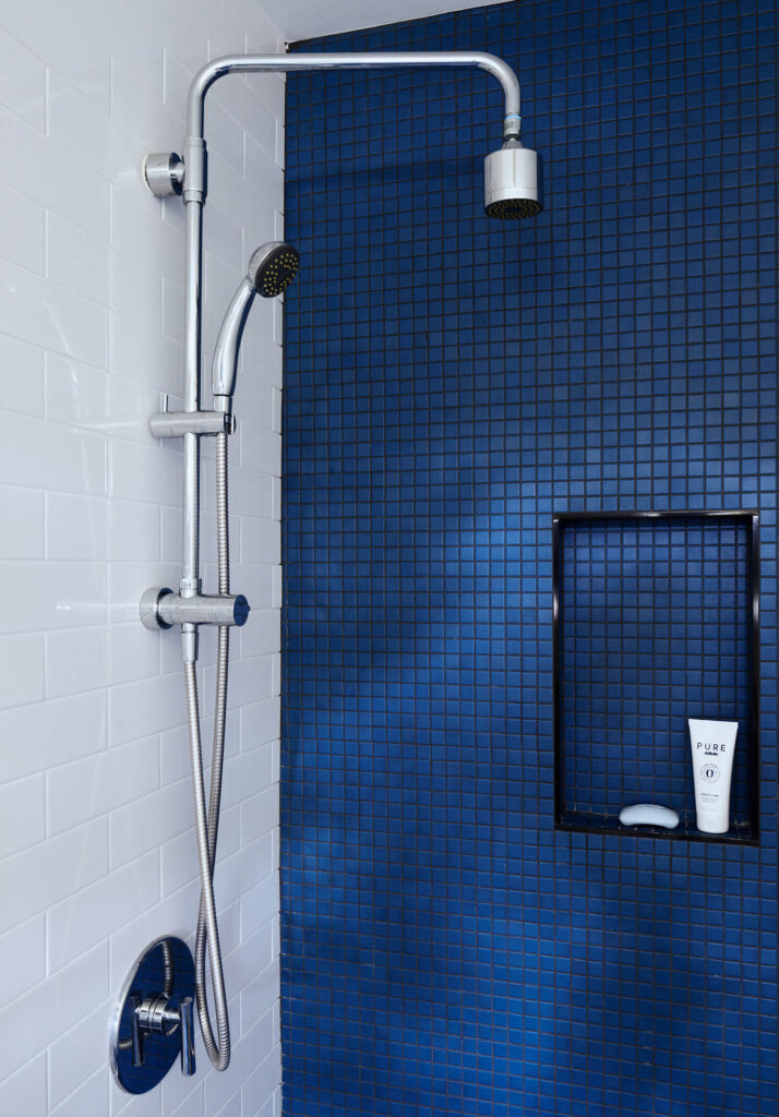 Modern kid-friendly bathroom with bold blue accent wall, white subway tile, and exposed plumbing at a historic Hingham home renovation.