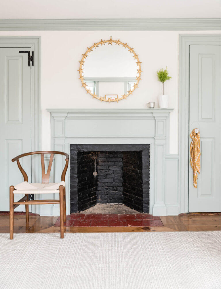 A 200-year-old Federal-style fireplace, refreshed with paint, sits alongside a plaid rug and a mid-century walnut Wegner chair.