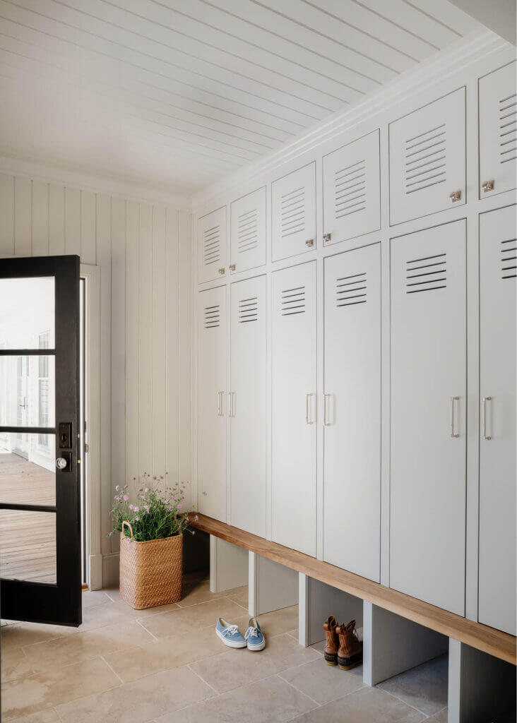 Custom light grey mudroom cabinets with a walnut bench, shiplap walls, limestone flooring, and a black door by a historic home designer in Hingham.