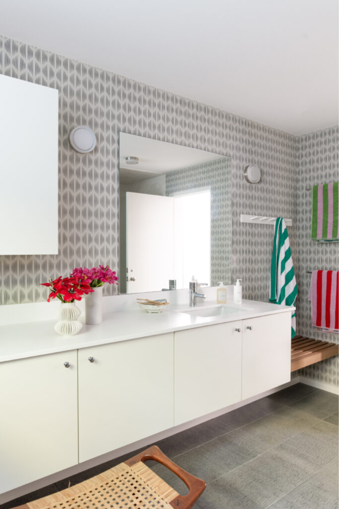 Kid-friendly bathroom with grey tile, white vanity, graphic Schumacher wallpaper, and colorful striped towels by an interior decorator in MA.