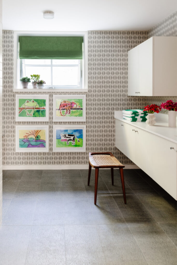 Kid-friendly bathroom with grey tile, white vanity, Schumacher wallpaper, green window shade, kids’ art, and striped towels in a modern design.