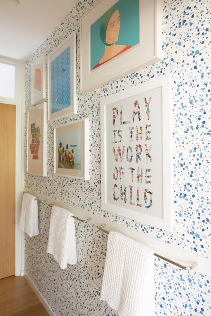 Kid-friendly bathroom with Hinson splatter wallpaper, colorful art, natural white oak flooring, and door in a new construction home.