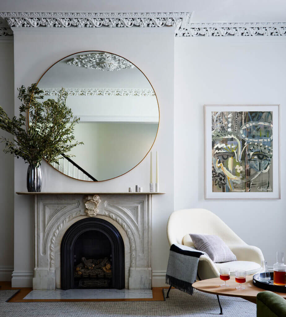 An original marble fireplace in a Boston brownstone sits beneath a modern mirror, paired with mid-century furniture and contemporary art.