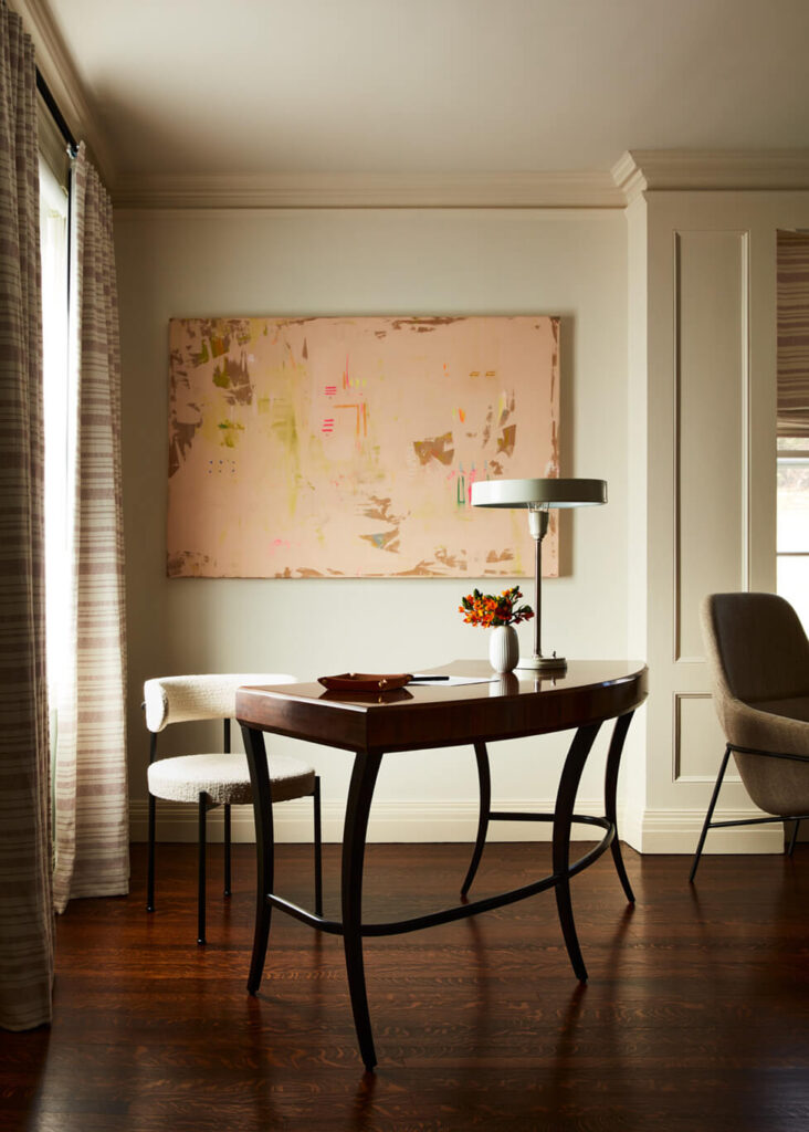 A vintage desk with modern chairs beneath contemporary art in a historic Concord home, designed by a Boston interior decorator.