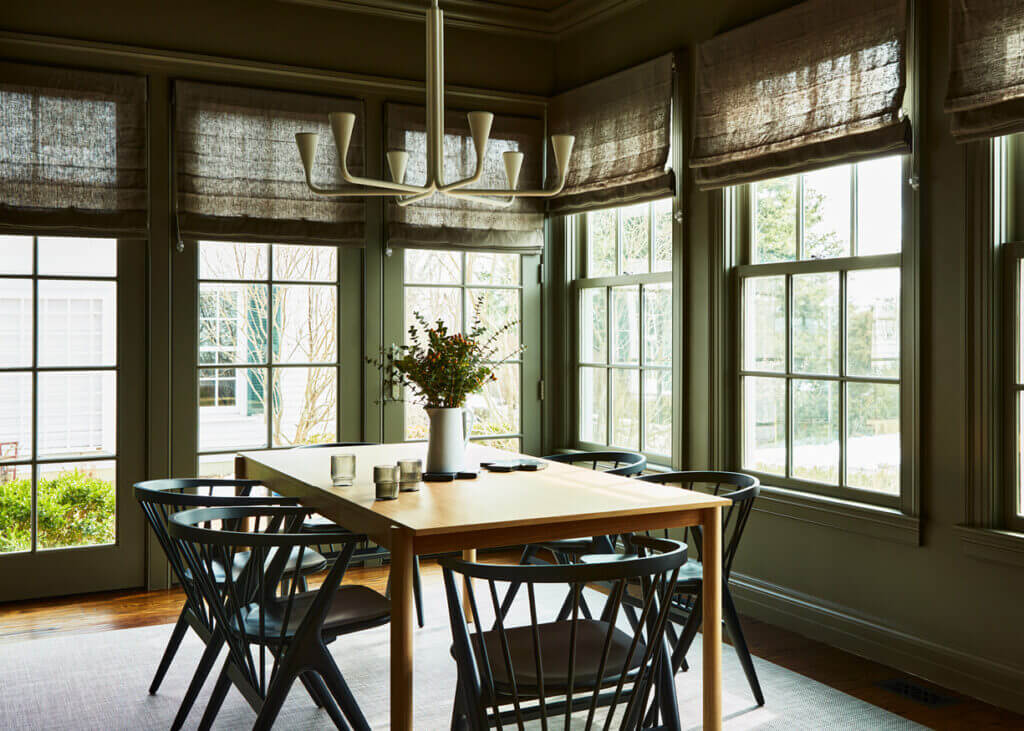 A taupe dining room with dark walls, a white plaster fixture, an oak table, and black spindle chairs in a historic Concord home by a Boston interior decorator.