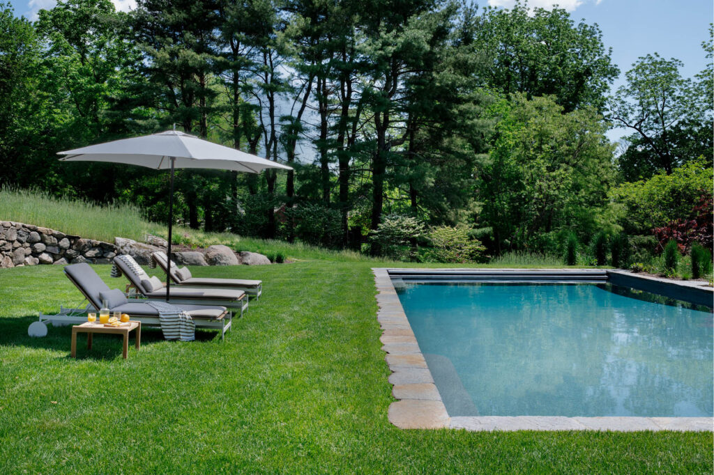 Modern pool with granite surround, fresh grass, and modern furniture at a historic Concord home by interior designers in Boston.