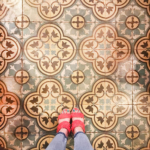 Historic concrete tiles in green, yellow, and brown patterns in Havana, Cuba, with Sarah Scales wearing red fringe espadrilles.