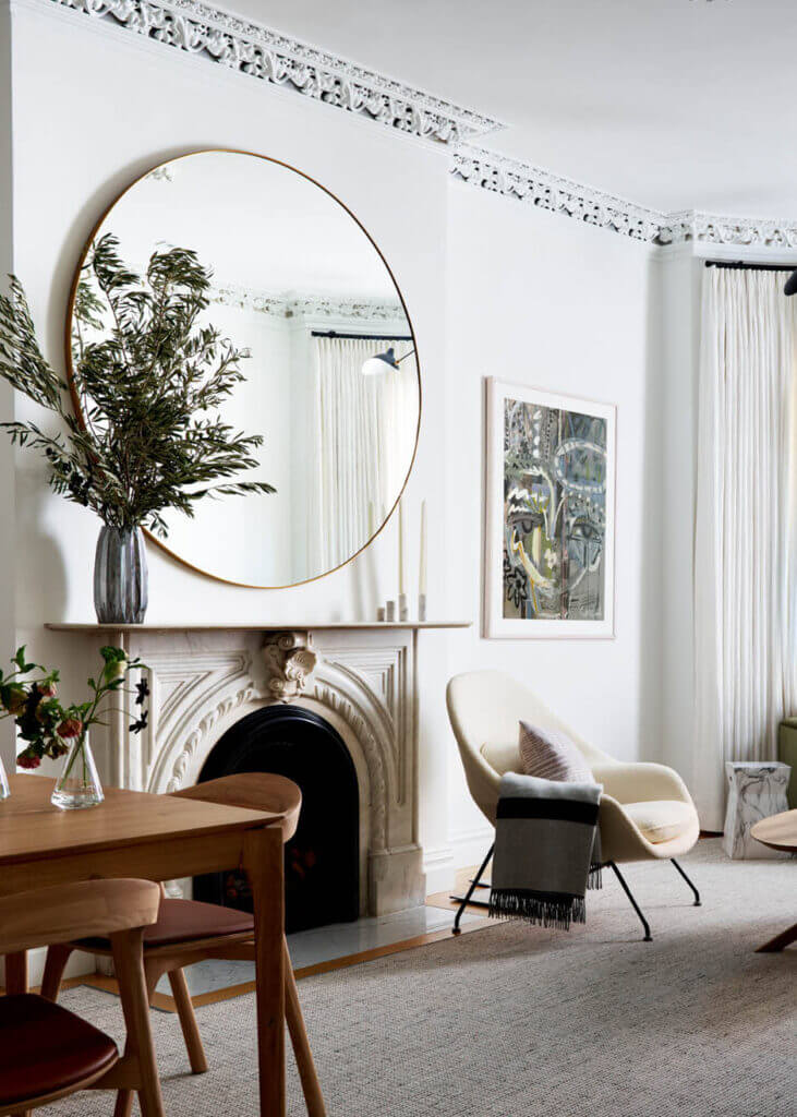 An original marble fireplace in a historic Boston brownstone pairs with a modern mirror, mid-century furniture, and contemporary art.