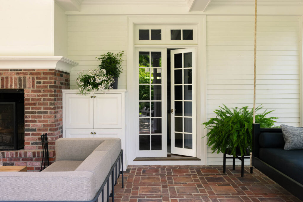 Original French doors with brick pavers, black hanging daybed, and modern furniture at a historic Concord home by a Boston interior decorator.